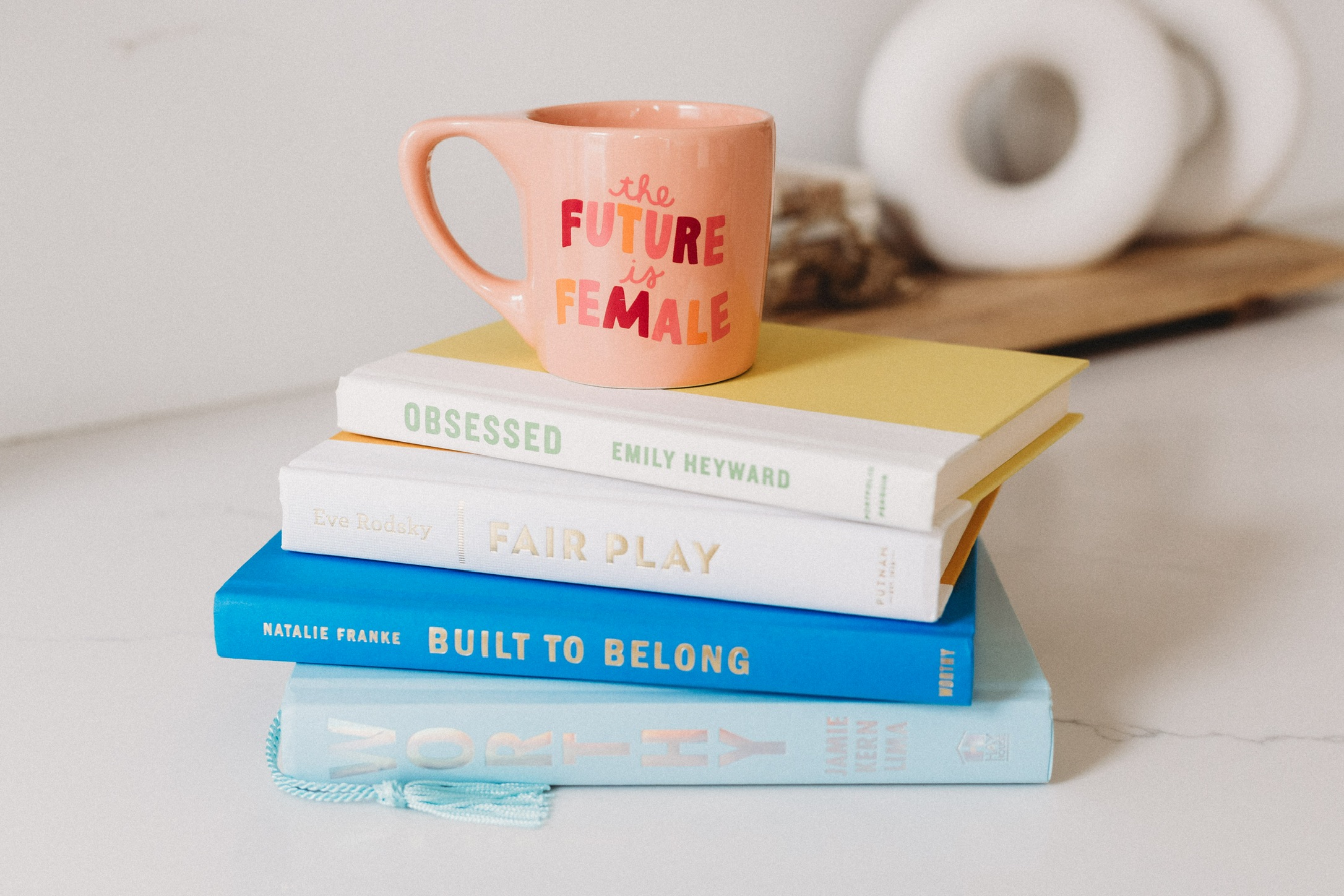 Pink "The Future Is Female" mug on a stack of books by women authors on a white counter