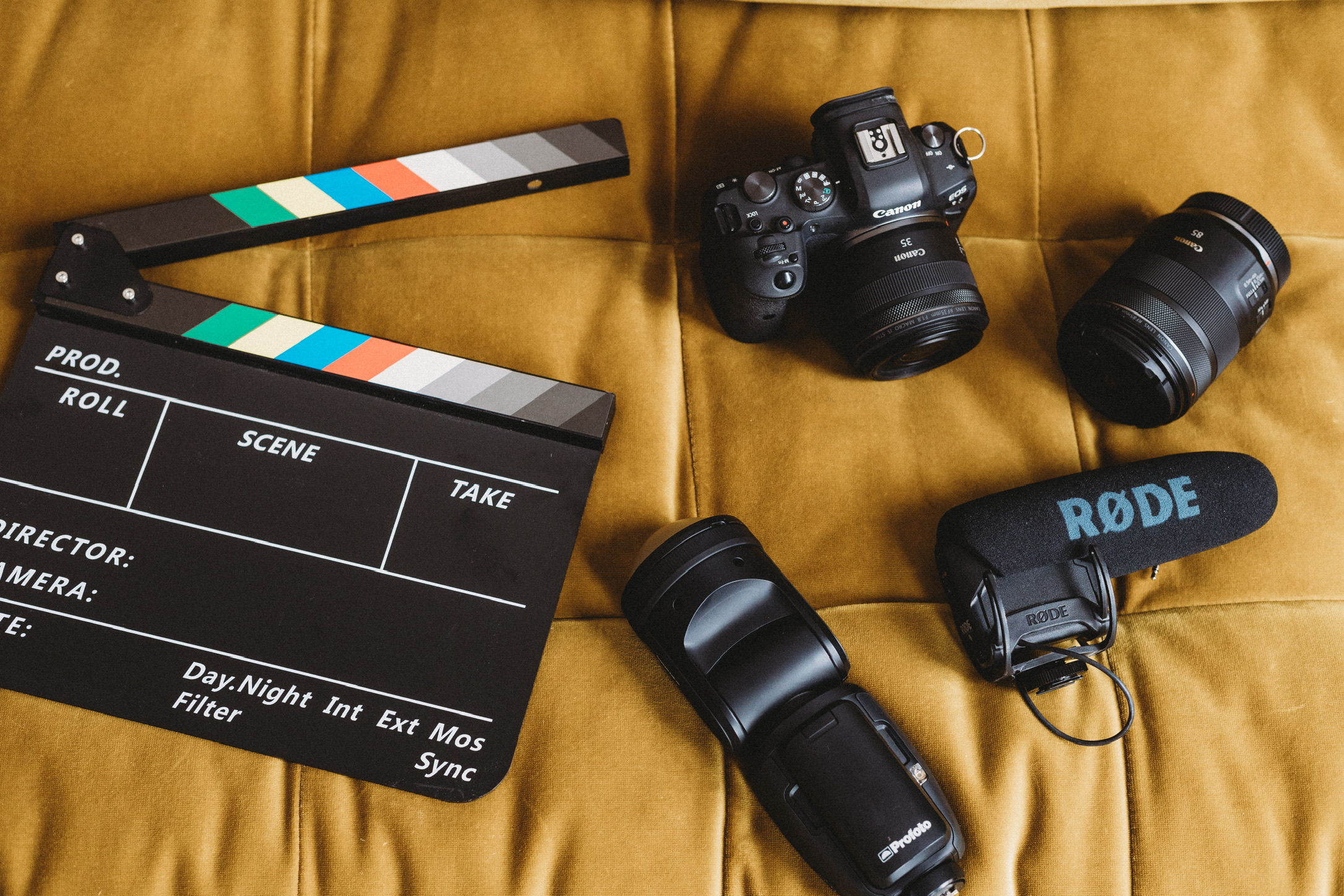 Flat lay of cameras, lenses, a Rode mic and a clapperboard on a mustard blanket, set up for a brand photoshoot