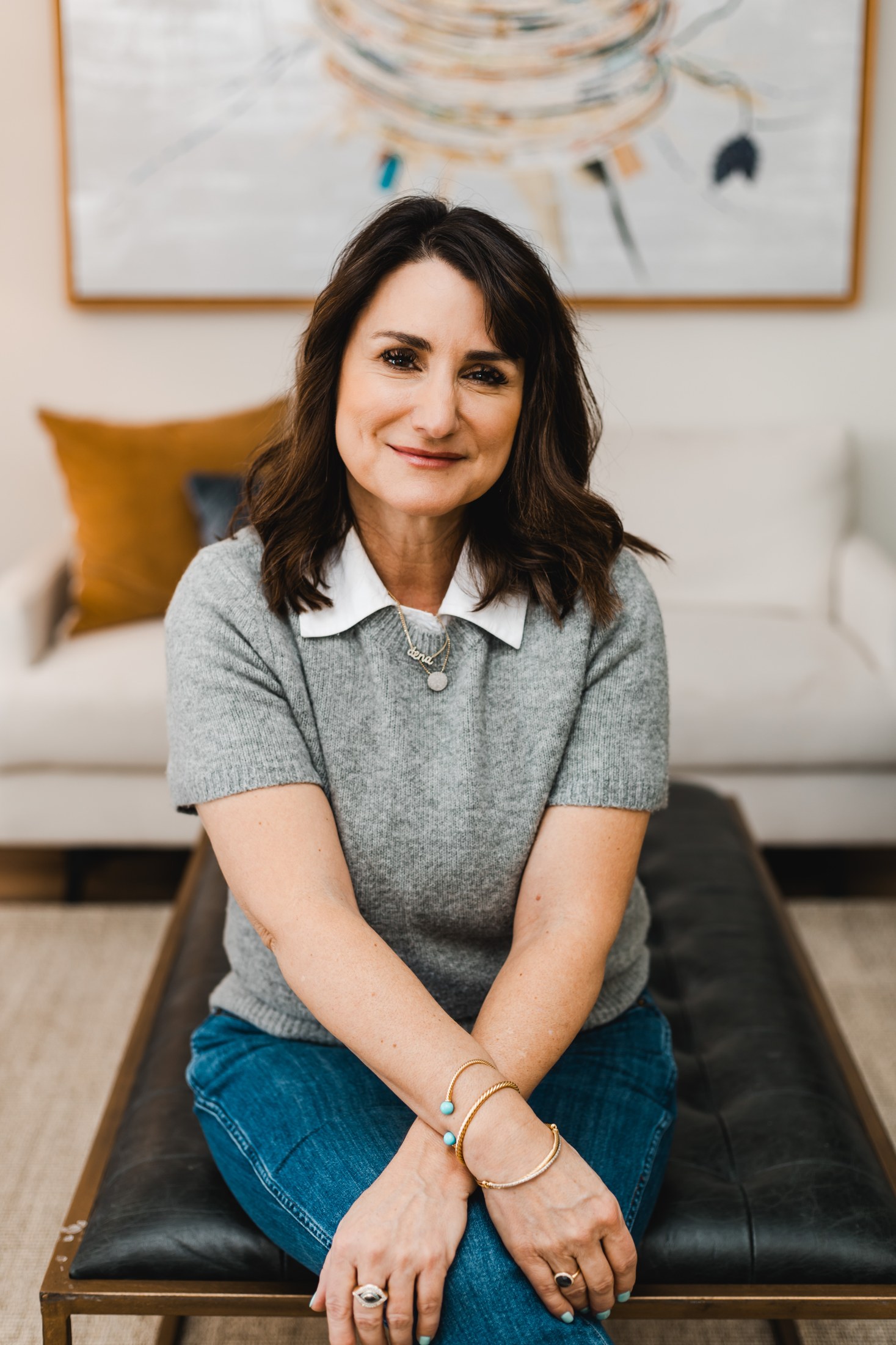 Woman business owner in a gray sweater seated on a leather bench, smiling at the camera during her Indianapolis brand photo session